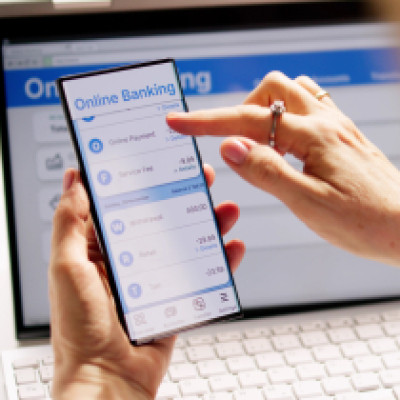 Person using a smartphone and laptop for online banking vs mobile banking comparison.
